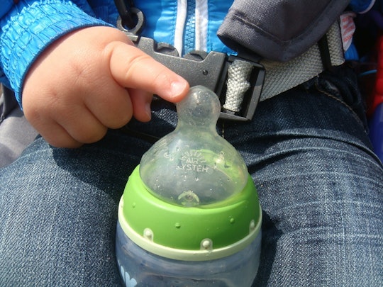 A toddler sitting in a car seat with a baby bottle full of soy milk in his lap.