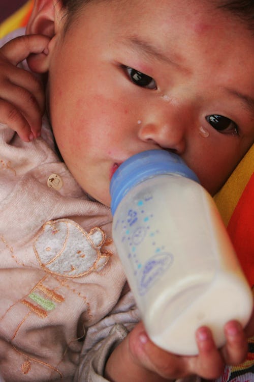 A baby in a pink shirt holding a bottle full of milk and drinking from it