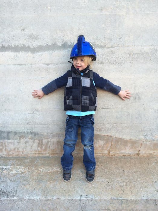 A toddler with a blue helmet on his head leaning to a wall