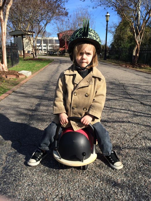 A toddler with a helmet on his head riding a toy car in a park