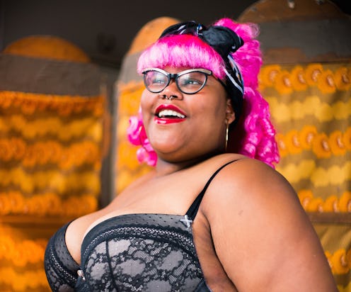 Natalie Deltonya with horn rimmed glasses pink hair and in a black bra