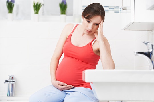 A pregnant woman in a red top with pregnancy hemorrhoids sitting on the edge of a bathtub