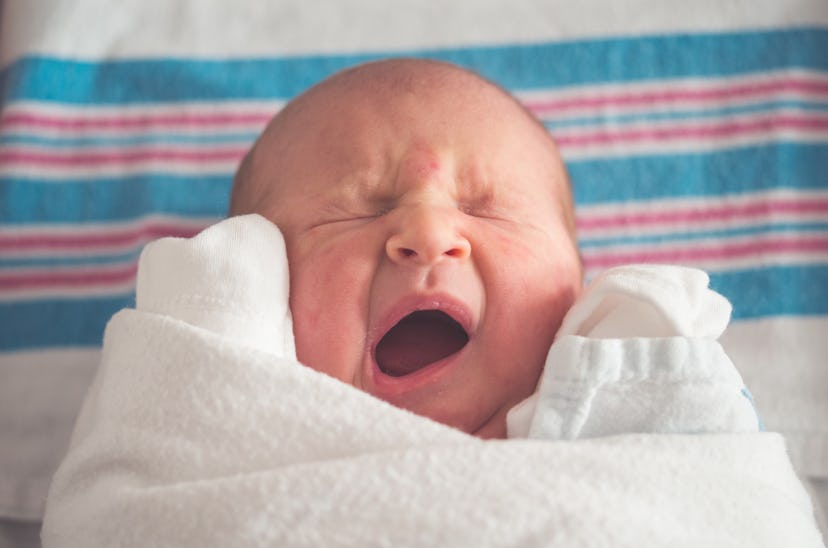 A baby swaddled in a white sheet yawning