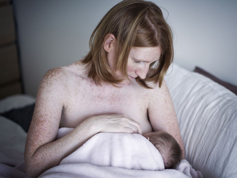 A woman sitting on a bed while breastfeeding her newborn child
