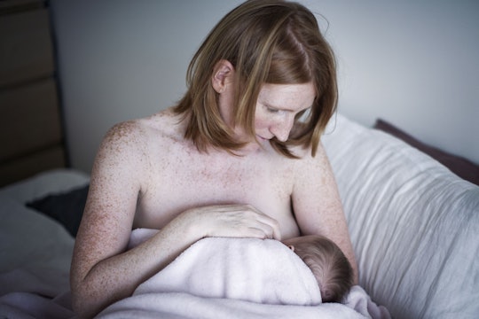 A woman sitting on a bed while breastfeeding her newborn child