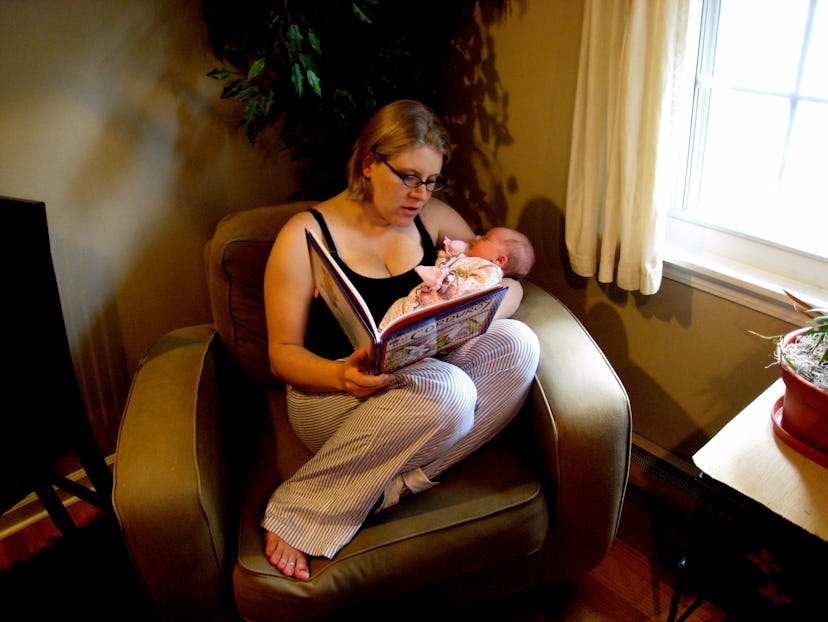 Mother holding her baby while sitting in a chair and reading a book