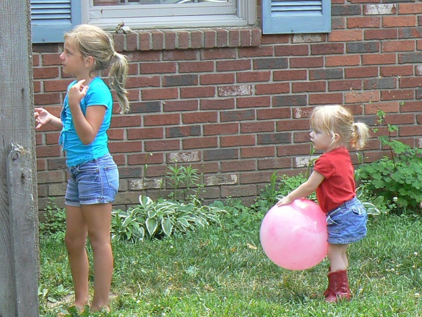 Two little sisters playing outside, where one of them has a pink balloon in her hand
