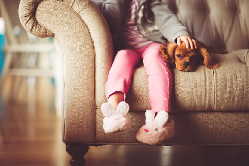 A little girl sitting at home on a couch and cuddling her dog