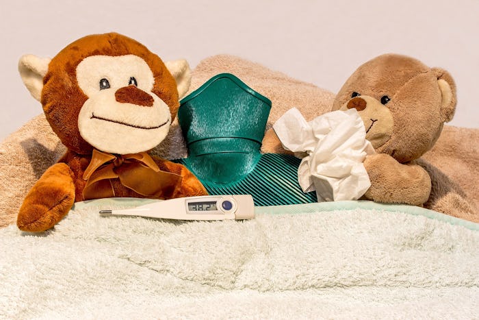 Two teddy bears, a green heater, and a thermometer on a bed