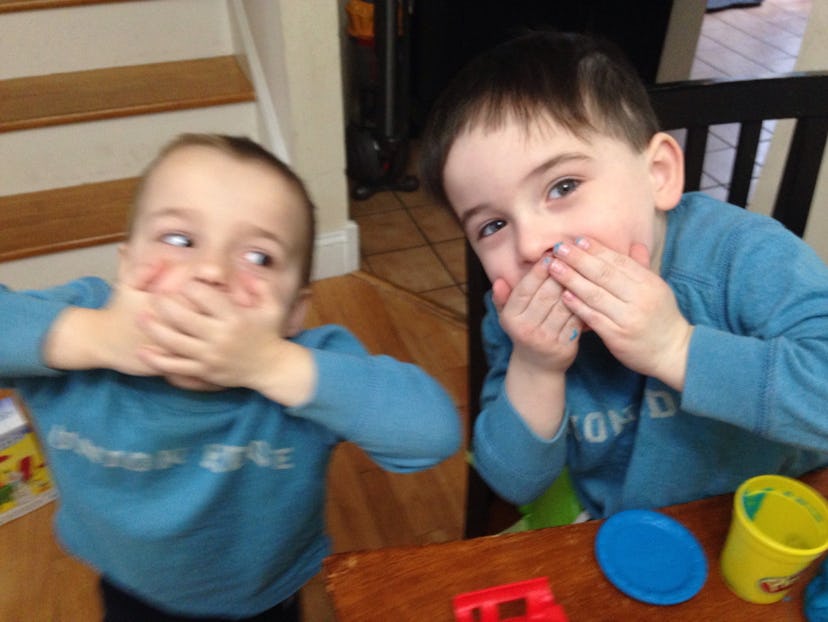 Two little brothers in blue shirts closing their mouths with their hands