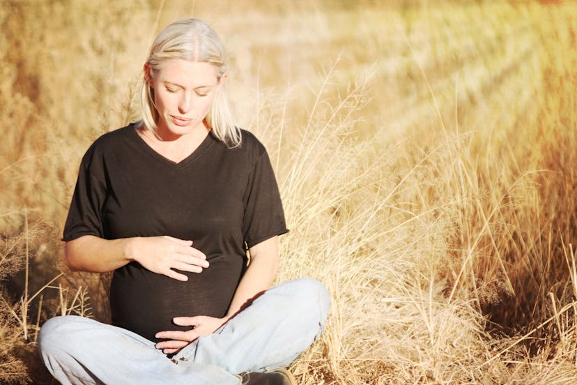 Blonde pregnant woman sitting on ground in the middle of a field