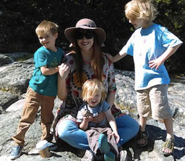 A mother posing for a photo with her three young kids
