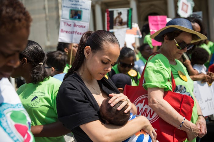 A woman on the street in a crowd, breastfeeding her baby