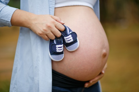 A mom with a pregnant stomach holding tiny newborn shoes next to her stomach