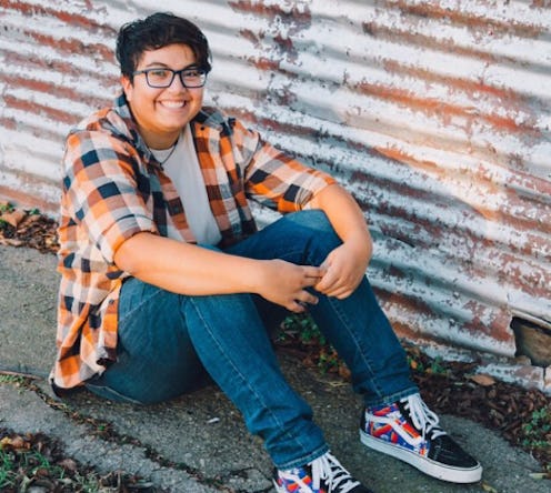 Daniel Suarez, a trans man, wearing a checked shirt over a white t-shirt, denim jeans and Vans shoes...