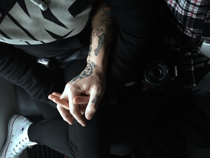 A close shot shows people holding hands, whereas one of the hands is tattooed.