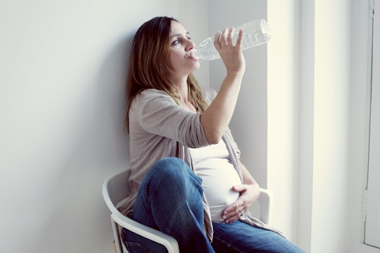 A pregnant woman drinking water from a bottle while holding her belly.