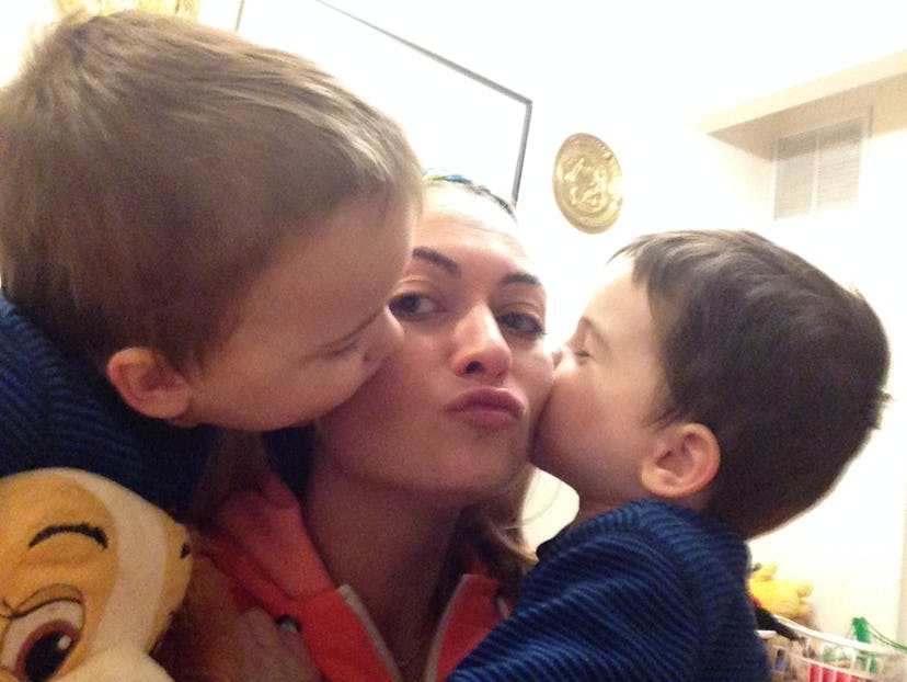 A mother taking a selfie with her two sons, who are giving her kisses