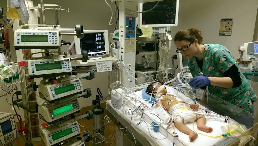 A baby in a hospital connected to machines with the nurse standing next to him.