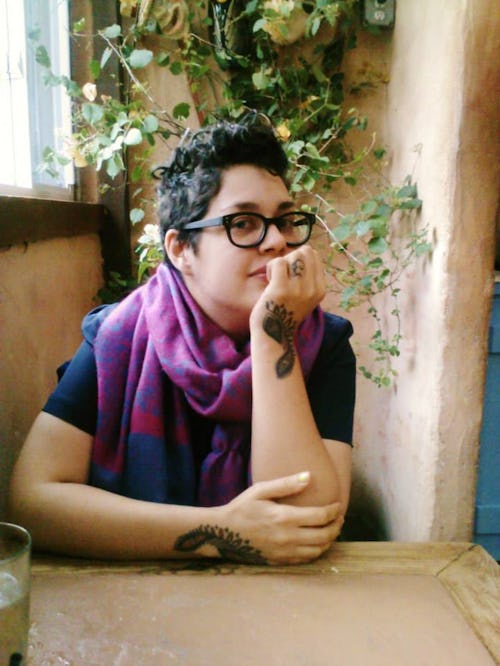 A non-binary mom posing for a photo wearing a purple scarf and glasses 