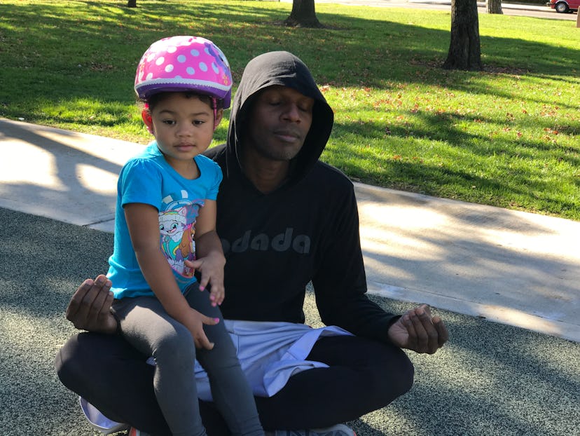 A dad with depression meditating in the park while his daughter sits in his lap