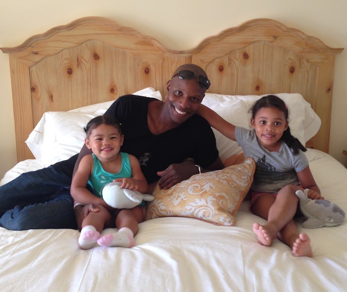 A dad with depression sitting on a bed next to his two daughters.