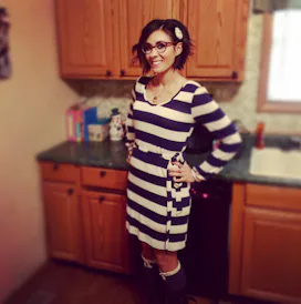 Mother with an eating disorder in a striped dress standing in her kitchen and smiling