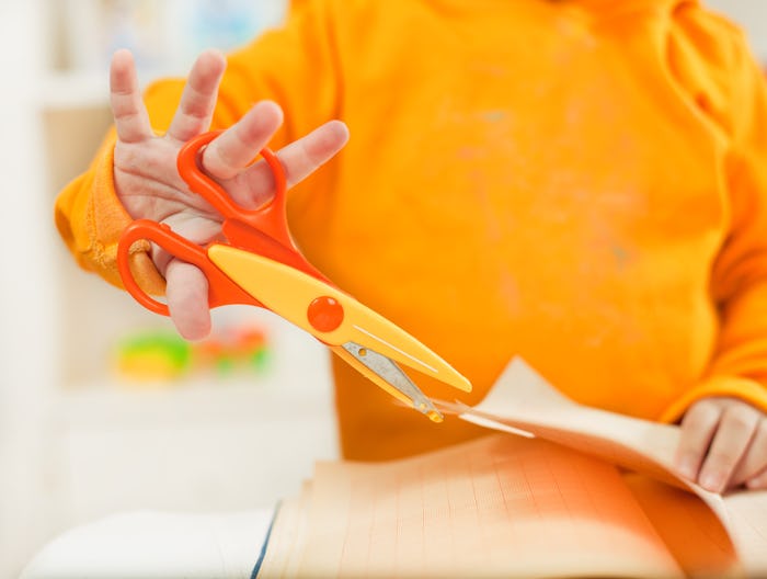 Kid in yellow sweater using safety scissors to cut a page out of a book