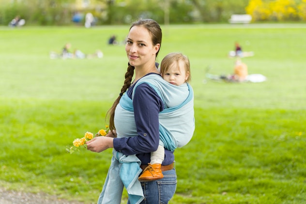 A young mother holding her baby in the backpack carrier, posing for the picture while having a fun o...
