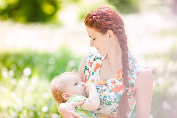 A mother in a floral dress breastfeeding her baby in a field