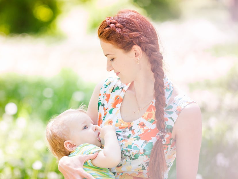 A mother in a floral dress breastfeeding her baby in a field