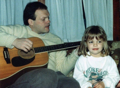 Image of young Claire sitting  in the living room while her father plays the guitar
