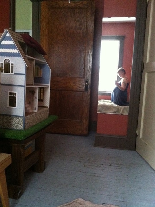 A woman who has prenatal depression taking a selfie in a mirror in a child's room with a doll house