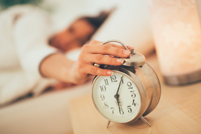 A woman lying in bed reaching over to stop her alarm clock from ringing
