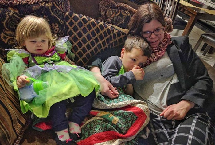 A mother lying on couch with her two kids and watching television