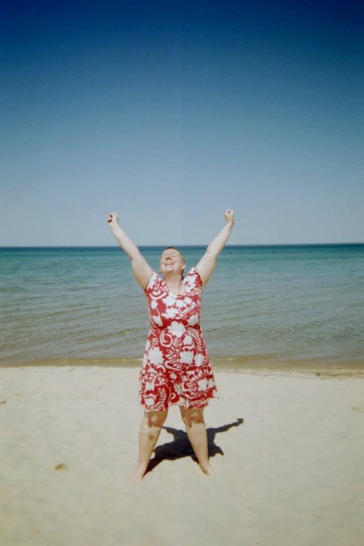 Katherine DM Clover raising her arms while standing on a beach in a floral dress