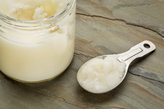 A jar and a tiny metal spoon with coconut oil on a marble surface