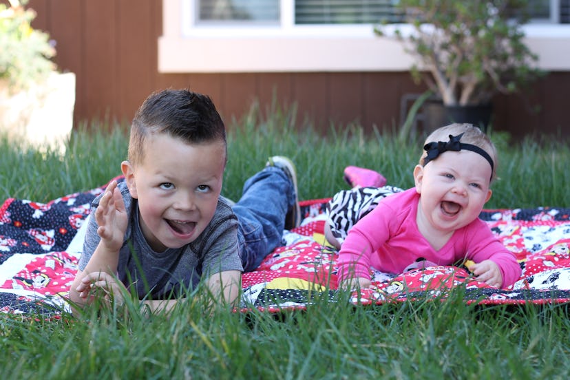 Two little siblings laying outside on the ground having fun with each other
