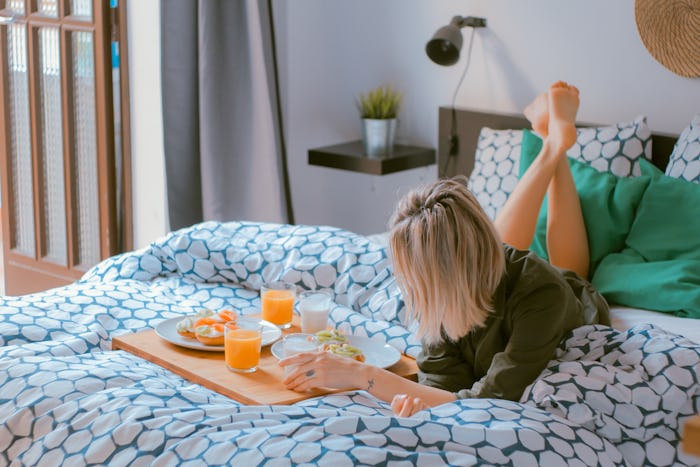 A mom lying stomach down on a bed and eating breakfast while she has the house to herself