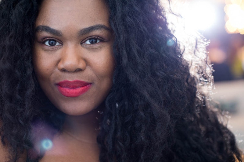 A Millennial woman with a black curly hair wearing a red lipstick 