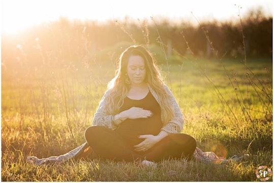 A pregnant woman holding her belly while sitting in a field