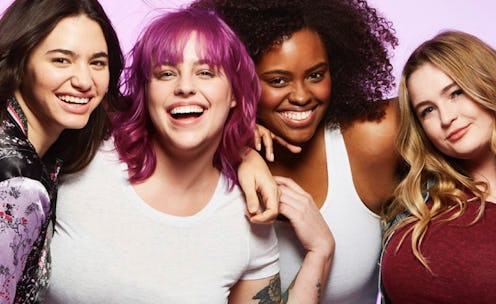Four girls standing together hugging and smiling in front of a pink background