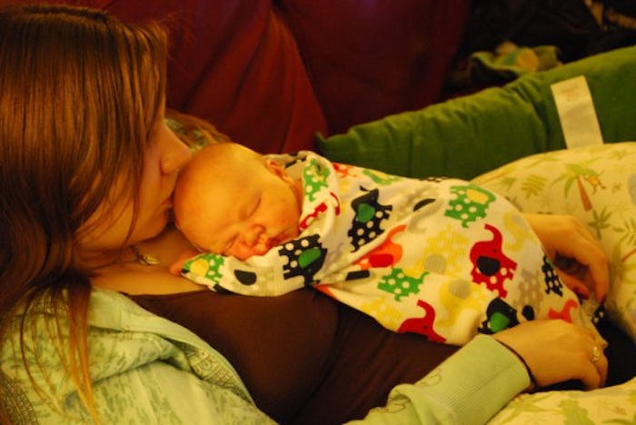 A mother lying on a couch while her baby is taking a nap on her chest during the day