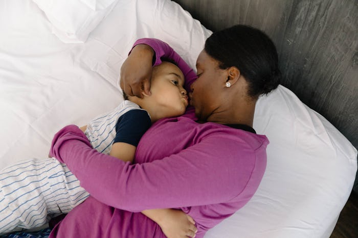 Mom in a purple shirt holding her child on the bed and kissing him