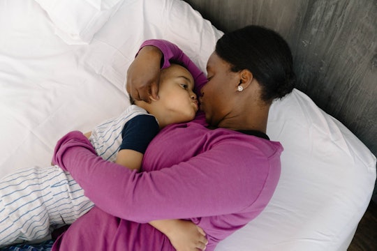 Mom in a purple shirt holding her child on the bed and kissing him