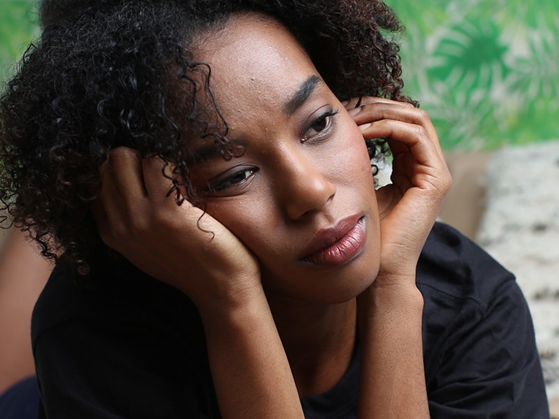 A curly-haired woman with Lupus lying stomach down and leaning her head on her wrists looking into t...