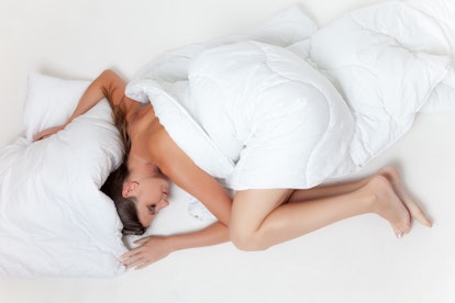 A pre-diabetic woman lying in bed covered by a white blanket experiencing fatigue
