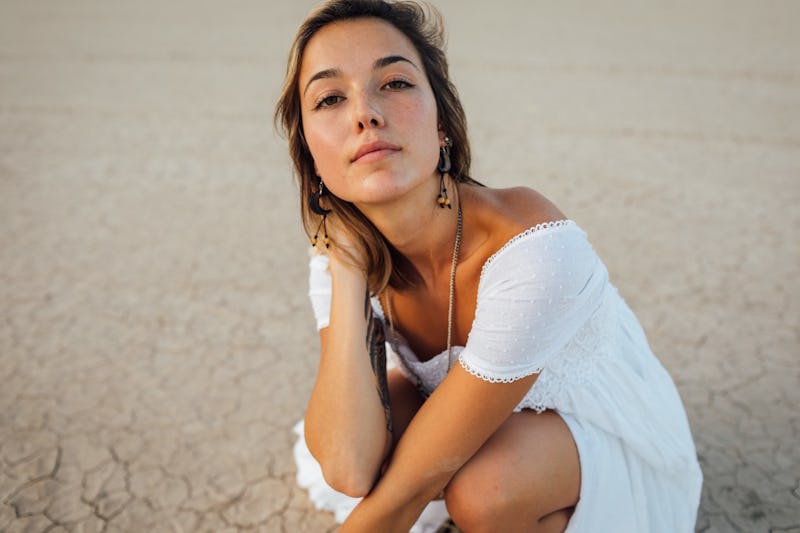 A pre-diabetic woman in a white dress crouching at the beach