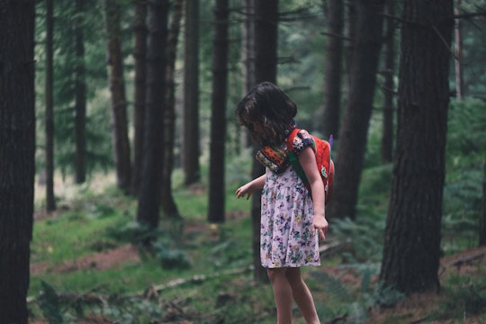 A little girl taking a walk in a forest in a floral dress and a red backpack