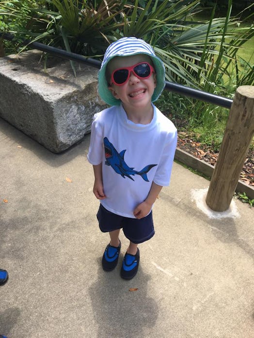 Little boy with red sunglasses and a hat, posing for a photo wearing a white t-shirt with a shark im...